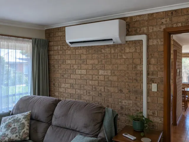 Wall-mounted split system above a brick feature wall in a living room with louvre open in Elizabeth East