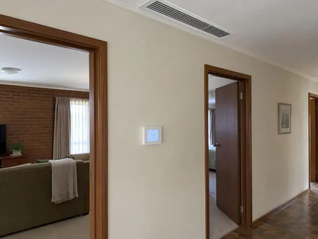 Hallway with ceiling ducted air vent and wall controller on a beige wall in a brick home in Elizabeth